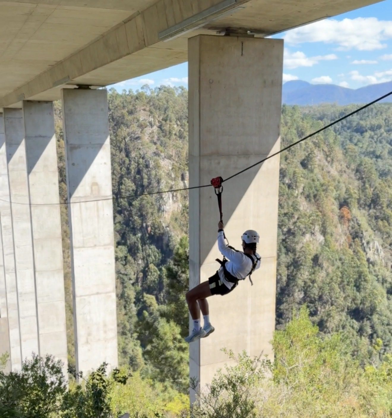 Rider crossing the gorge on the Bloukrans zipline beneath the bridge piers