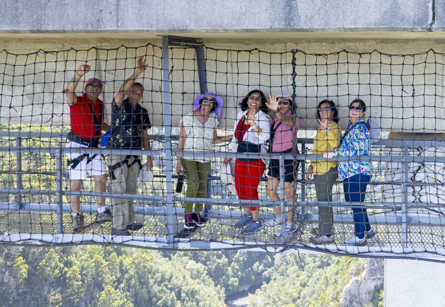 Group of visitors waving from the netted SkyWalk walkway beneath Bloukrans Bridge