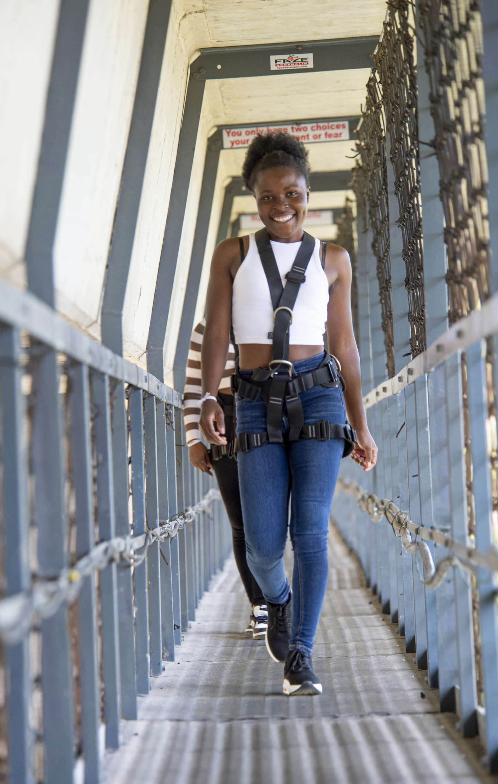 Jumper in a bungy harness walking the caged SkyWalk walkway beneath Bloukrans Bridge