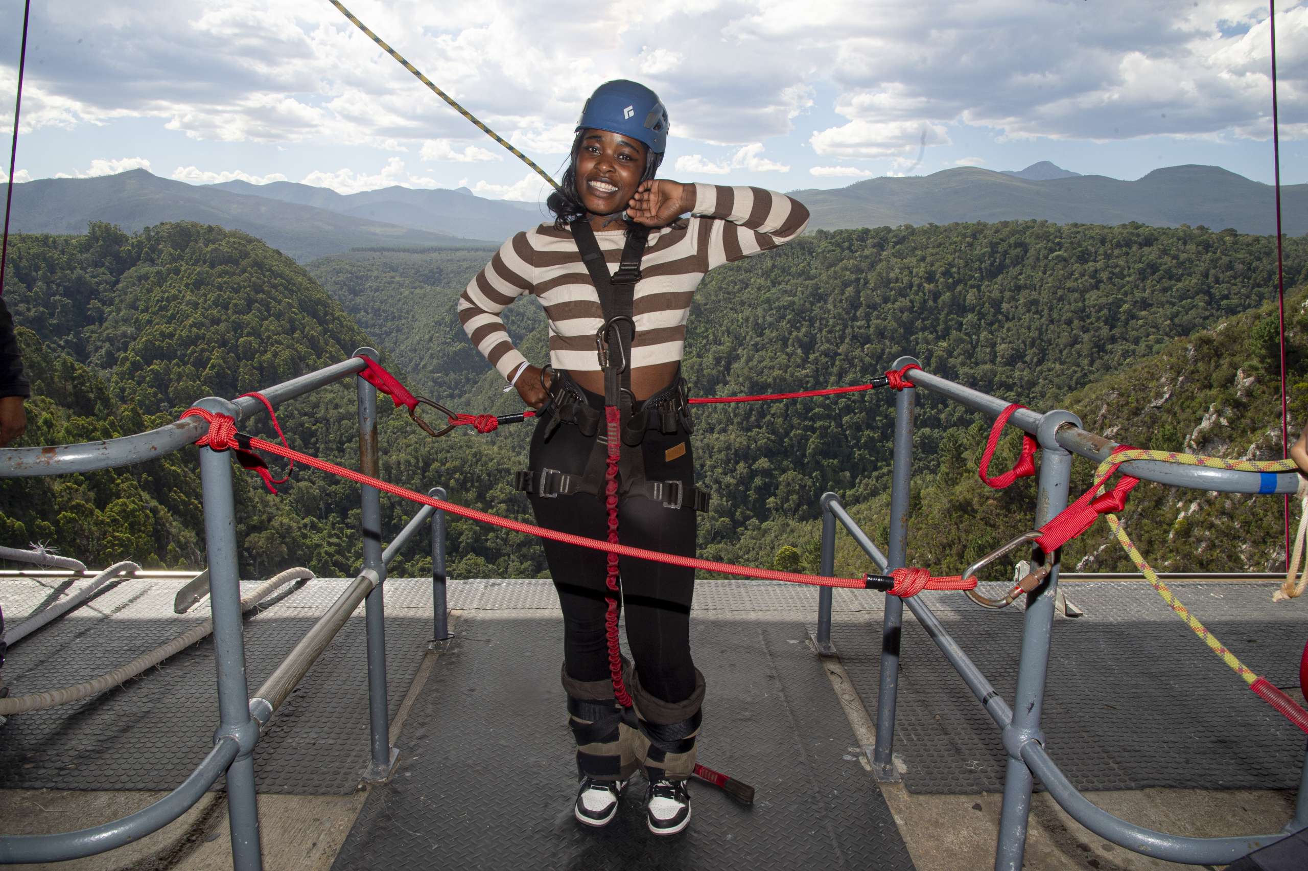 Bungy jumper in a helmet and ankle harness standing on the Bloukrans Bridge jump platform above the forested gorge